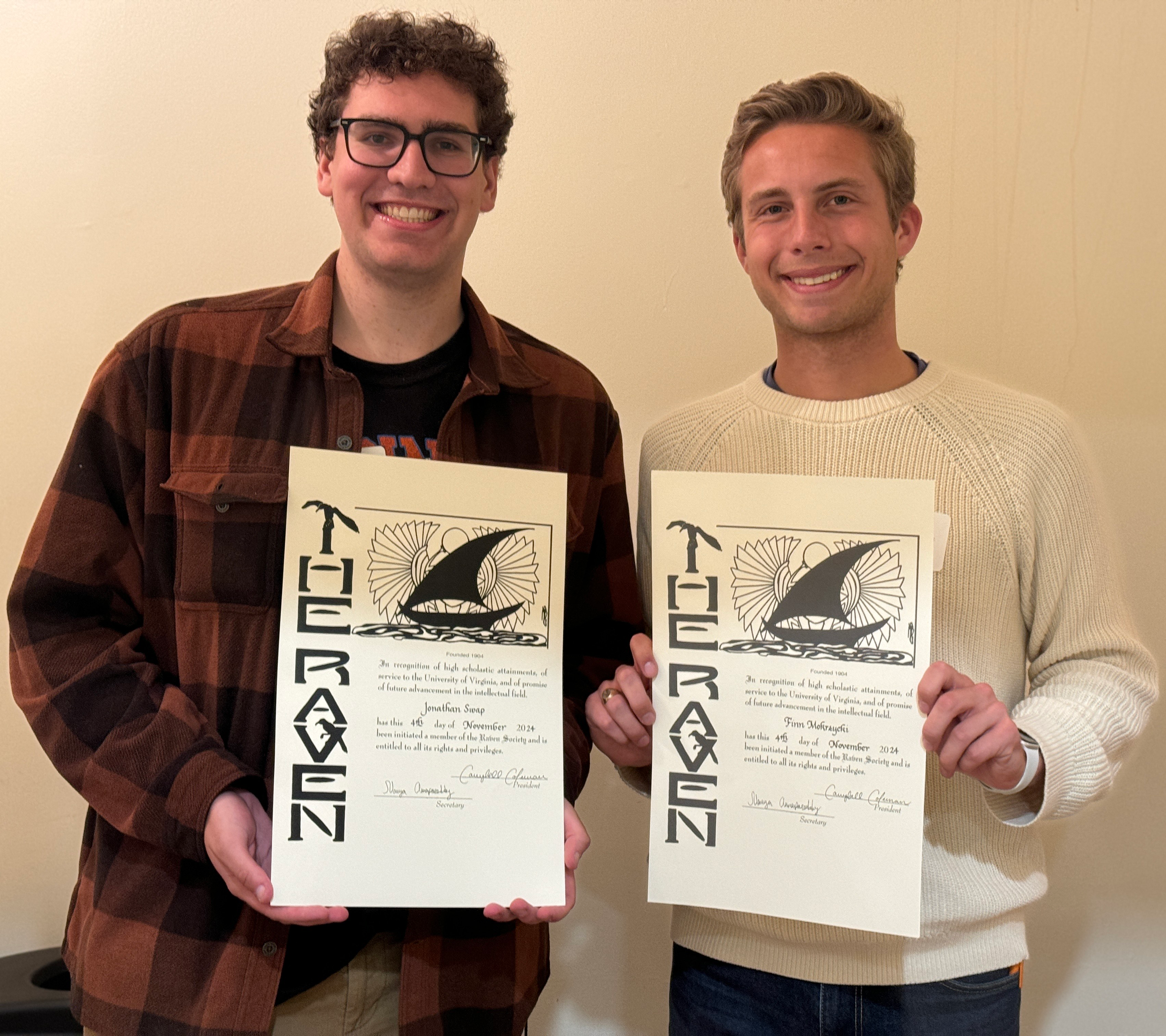 Two male students stand side by side with their Raven Society membership certificates