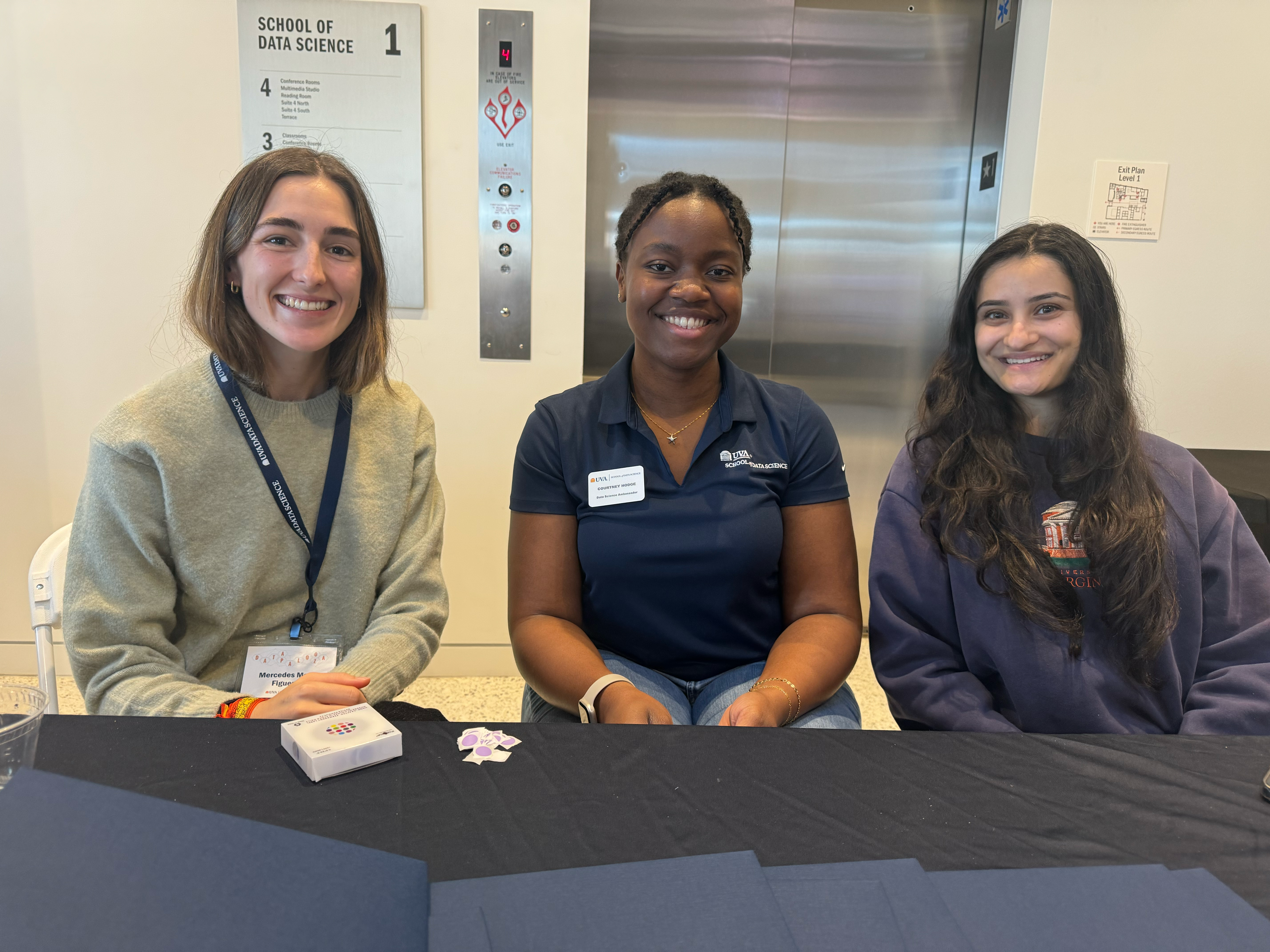 Three UVA Data Science MSDS Ambassadors at Datapalooza check in desk sitting side by side