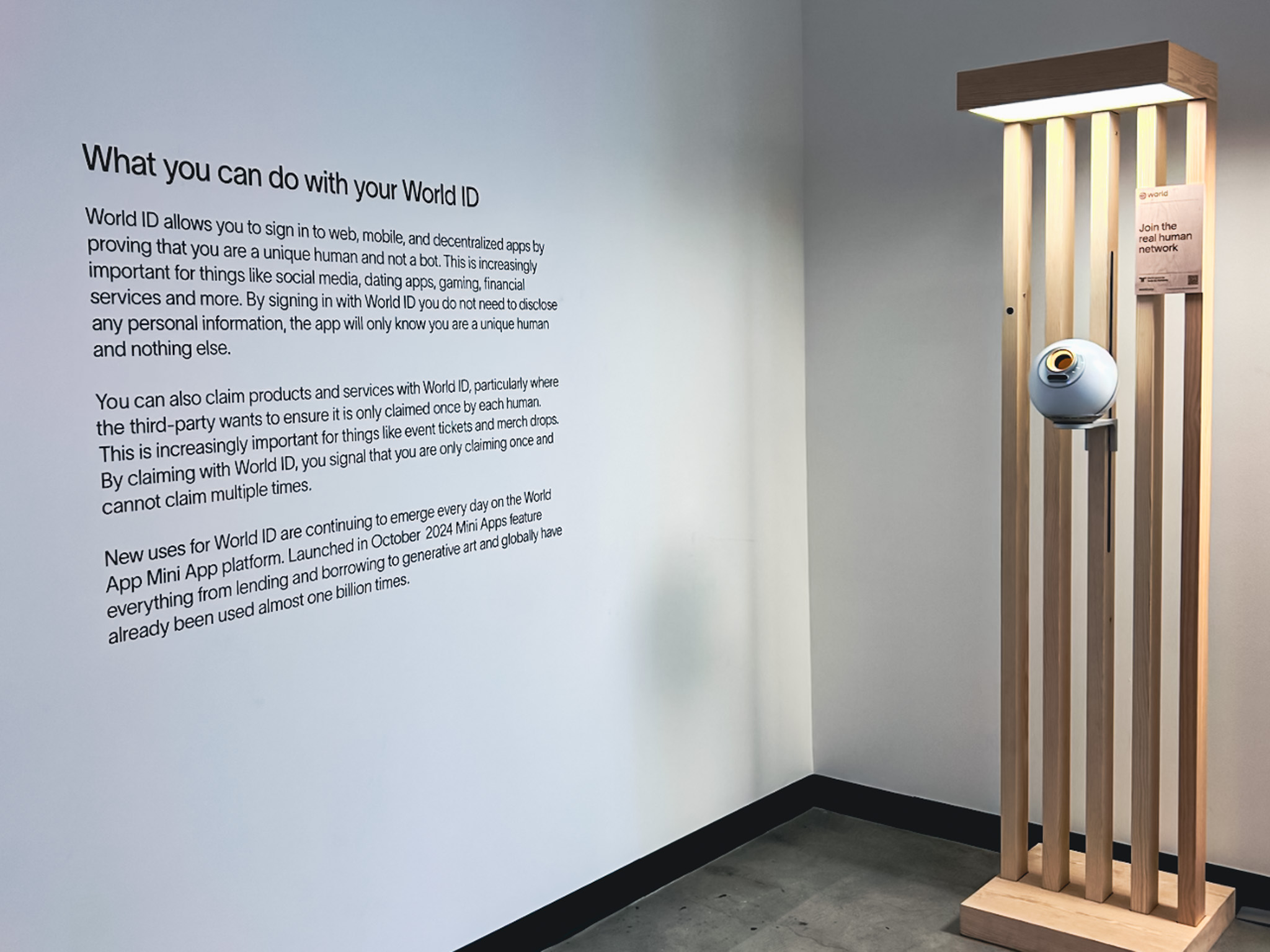 The Orb positioned on a wooden structure next to a wall that reads, "What you can do with your World ID."