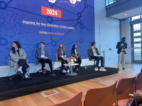 A panel moderated by Adam Tashman featuring other panelists inside of the School's Capital One Hub in front of a large digital screen.