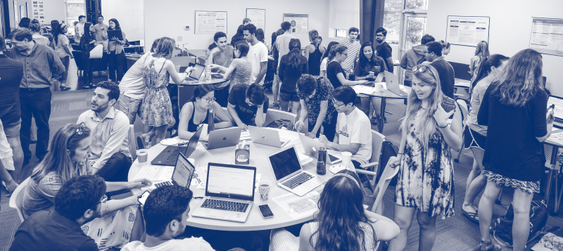 A lively room with diverse students engaged in collaborative group work around tables, using laptops for Data Viz Day.