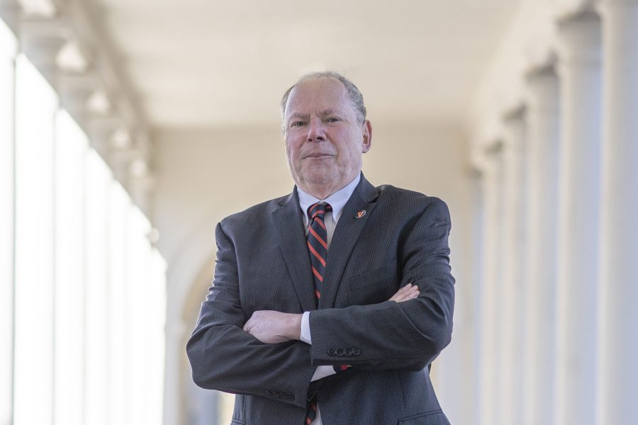 Phil Bourne, in a suit and striped tie, stands confidently with arms crossed in a column-lined hallway, conveying authority and professionalism.