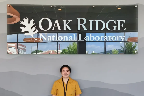 UVA Data Science MSDS residential student Christine George in a yellow shirt posing under the Oak Ridge National Labratory sign