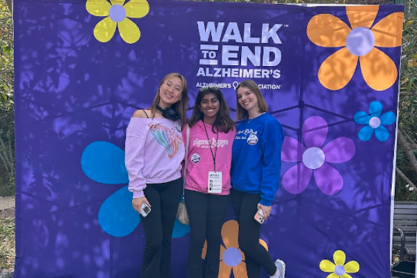 Three young women in front of a a purple banner with colorful flowers for Walk to End Alzheimers event